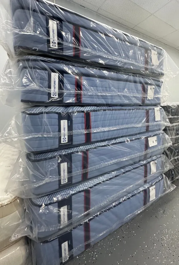 Stacks of wrapped Sealy Posturepedic mattresses on the warehouse floor, labels still attached