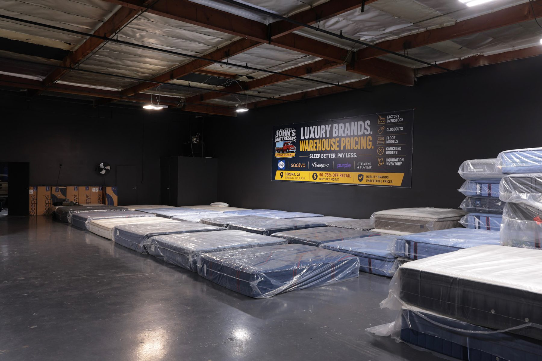 Interior de la bodega con el letrero de John's Mattresses que dice Luxury Brands, Warehouse Pricing