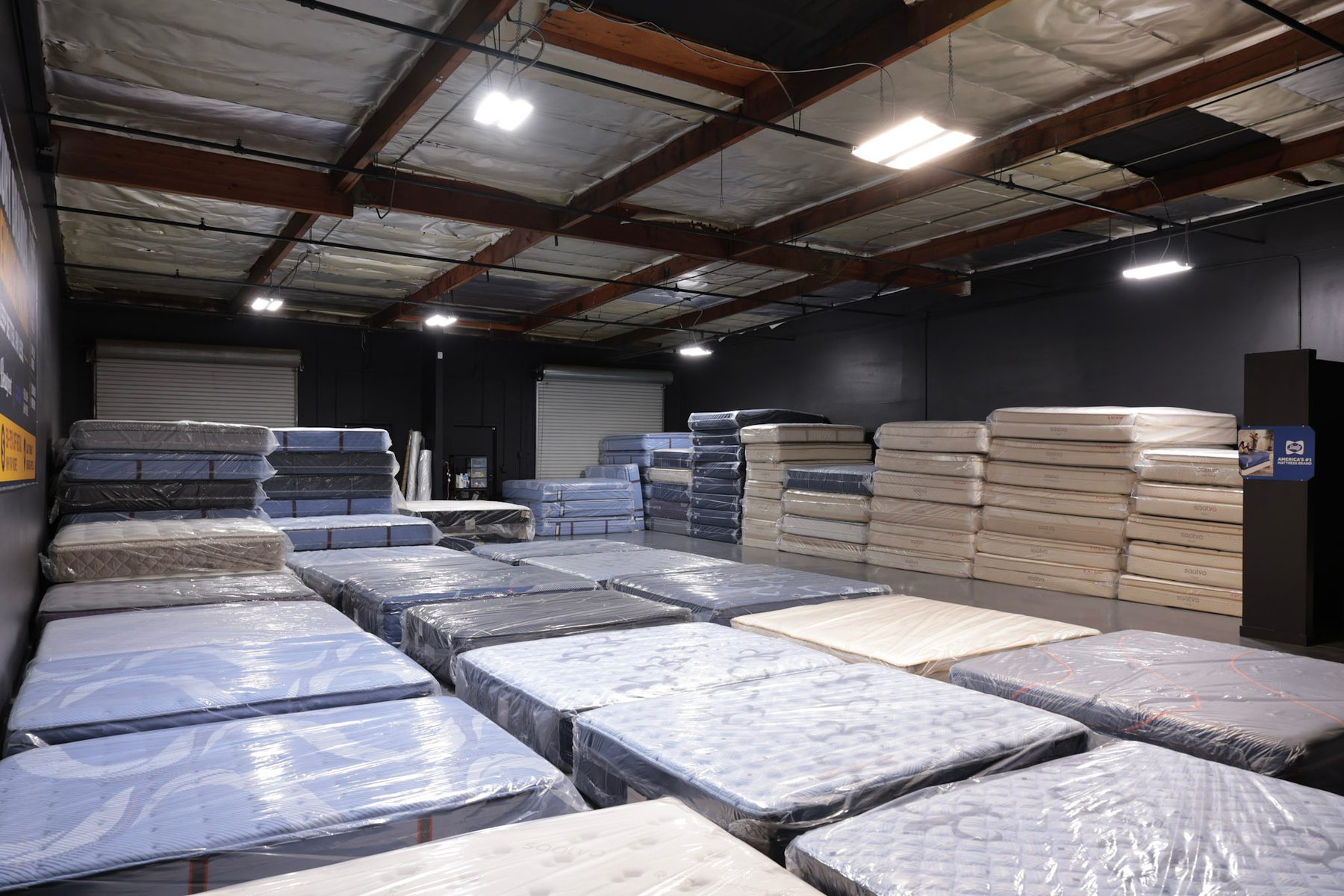 La bodega de John's Mattress Liquidation, filas de colchones envueltos en plástico con más apilados al fondo
